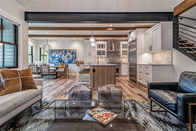 living room featuring sink, beamed ceiling, a notable chandelier, and light wood-type flooring