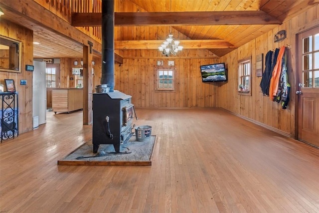 living room featuring a wood stove, wooden ceiling, an inviting chandelier, wooden walls, and light wood-type flooring