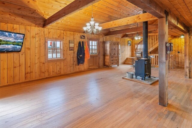 unfurnished living room featuring wooden walls, an inviting chandelier, wooden ceiling, light hardwood / wood-style floors, and a wood stove