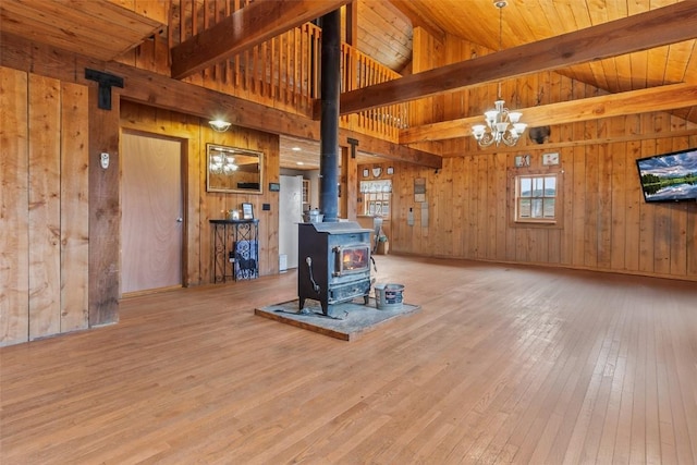 unfurnished living room with a wood stove, an inviting chandelier, wooden walls, light wood-type flooring, and beamed ceiling