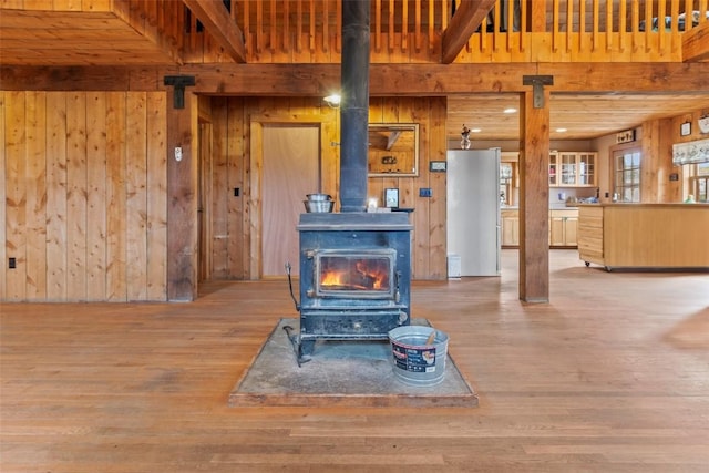 living room featuring hardwood / wood-style floors, a wood stove, beamed ceiling, and wooden walls