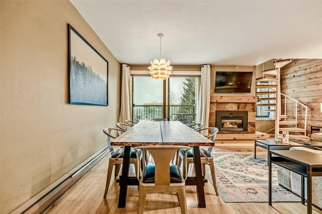 dining room with a chandelier, stairs, baseboard heating, a tile fireplace, and wood finished floors