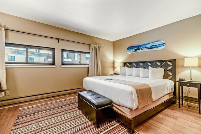 bedroom with multiple windows, light wood-style floors, and baseboard heating