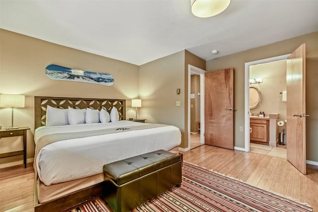 bedroom with ensuite bathroom, baseboards, and light wood finished floors