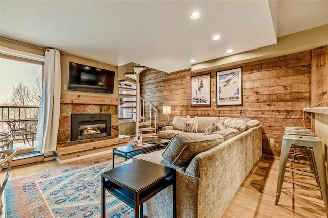 living room featuring wooden walls, plenty of natural light, wood finished floors, and a lit fireplace