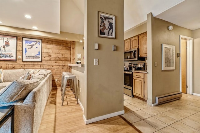 kitchen featuring light wood finished floors, open floor plan, stainless steel appliances, wood walls, and light countertops