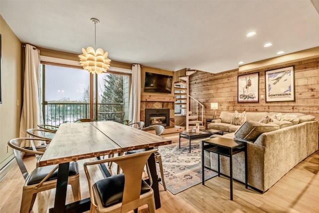 dining room featuring recessed lighting, a fireplace with raised hearth, wood walls, and light wood-type flooring