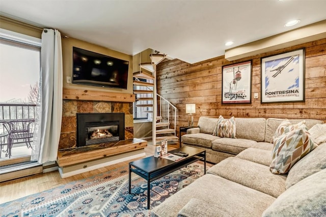 living room featuring stairs, a tiled fireplace, wood finished floors, and wood walls