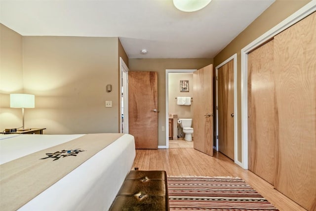 bedroom featuring connected bathroom, baseboards, two closets, and light wood-style flooring