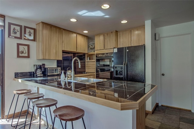 kitchen with kitchen peninsula, light brown cabinetry, tile counters, and black appliances