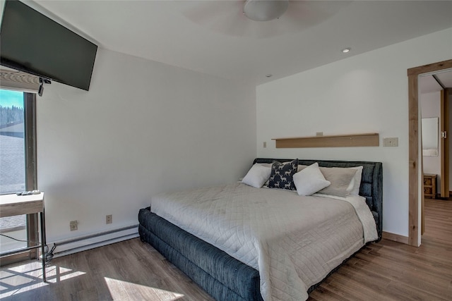 bedroom with hardwood / wood-style flooring, ceiling fan, and a baseboard heating unit