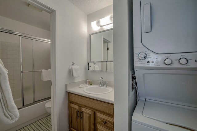 full bathroom featuring stacked washing maching and dryer, vanity, a textured ceiling, shower / bath combination with glass door, and toilet