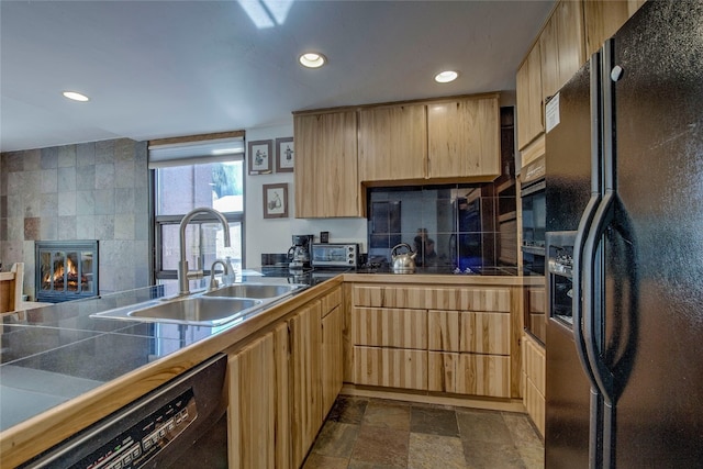 kitchen featuring kitchen peninsula, sink, black appliances, light brown cabinets, and a tiled fireplace