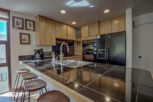 kitchen with black appliances, sink, light brown cabinetry, tile counters, and kitchen peninsula