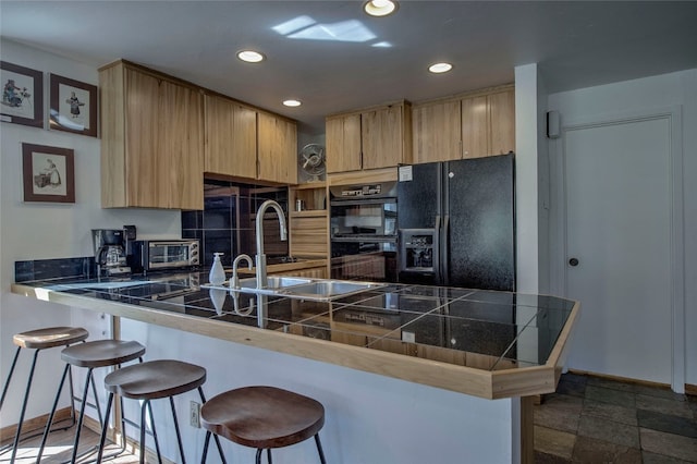 kitchen featuring tile countertops, light brown cabinets, black appliances, a kitchen bar, and kitchen peninsula