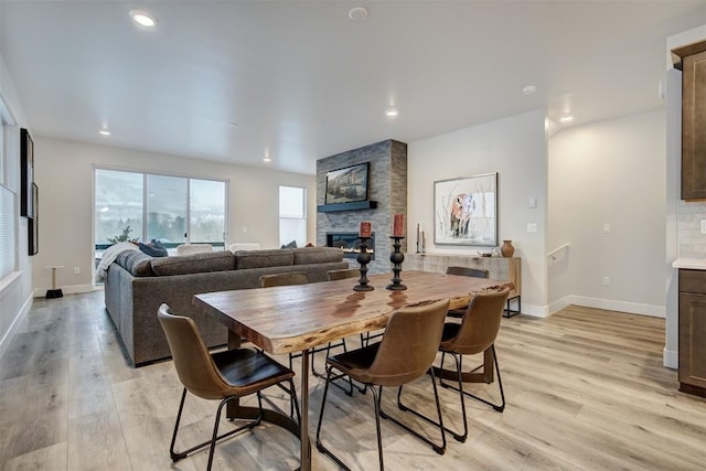 dining room featuring recessed lighting, baseboards, a stone fireplace, and light wood-style flooring