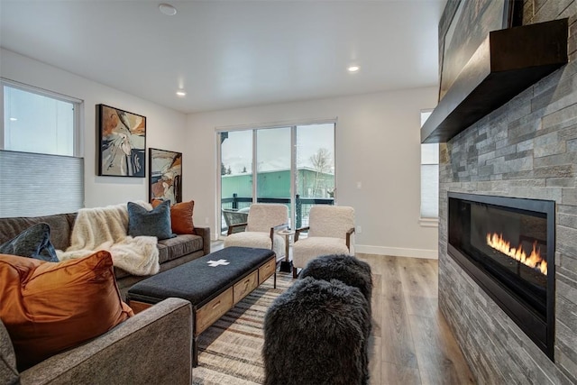 living area with a glass covered fireplace, recessed lighting, baseboards, and light wood-type flooring