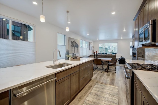 kitchen with light wood-type flooring, a sink, appliances with stainless steel finishes, tasteful backsplash, and open floor plan