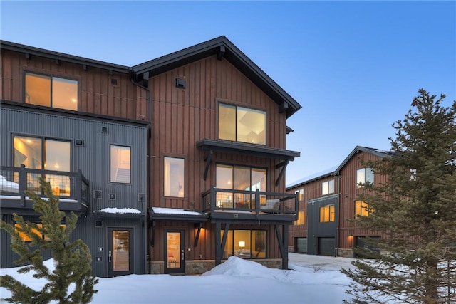 snow covered rear of property featuring a balcony and board and batten siding