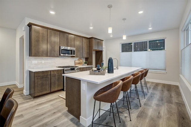 kitchen with a breakfast bar, light wood-style flooring, backsplash, and appliances with stainless steel finishes