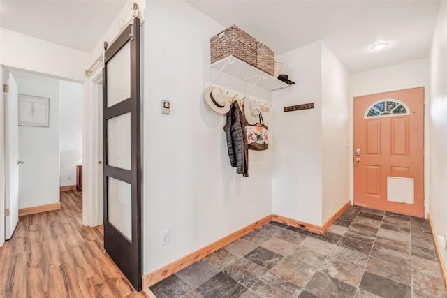 foyer entrance featuring a barn door, baseboards, and stone finish floor