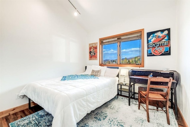 bedroom featuring vaulted ceiling, track lighting, baseboards, and wood finished floors