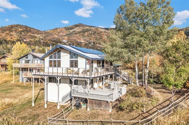 back of property with stairway, a deck with mountain view, a yard, roof mounted solar panels, and metal roof