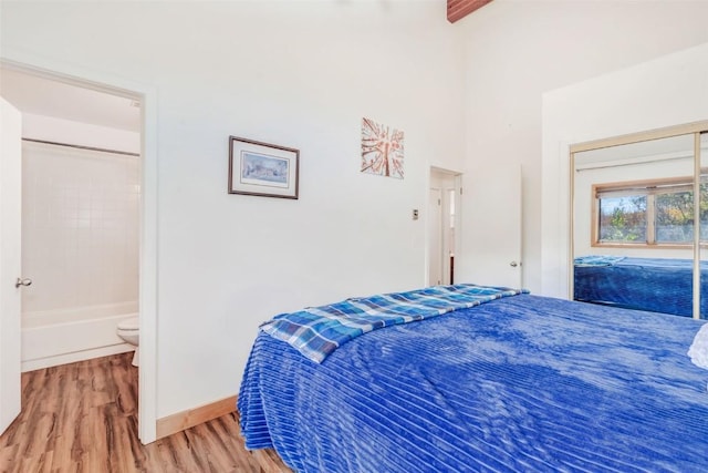 bedroom with baseboards, ensuite bath, a high ceiling, and wood finished floors