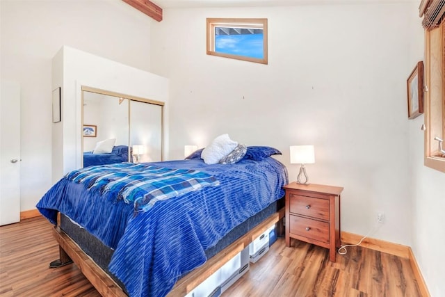 bedroom featuring lofted ceiling with beams, wood finished floors, a closet, and baseboards