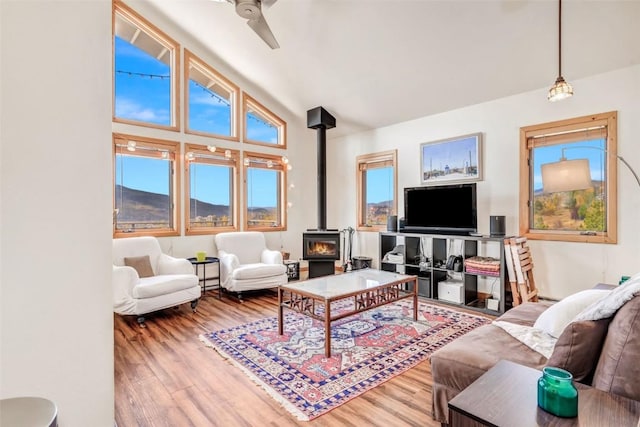 living area with lofted ceiling, a wood stove, wood finished floors, and ceiling fan