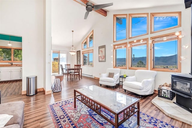 living room featuring high vaulted ceiling, a baseboard heating unit, wood finished floors, baseboards, and a wood stove