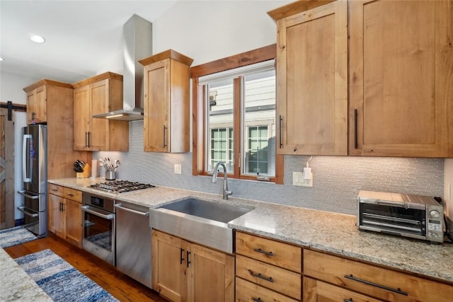 kitchen with a toaster, light stone counters, stainless steel appliances, wall chimney range hood, and a sink