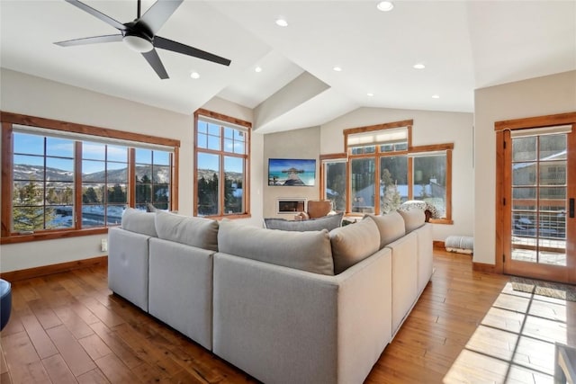 living room with a mountain view, wood finished floors, baseboards, vaulted ceiling, and a glass covered fireplace