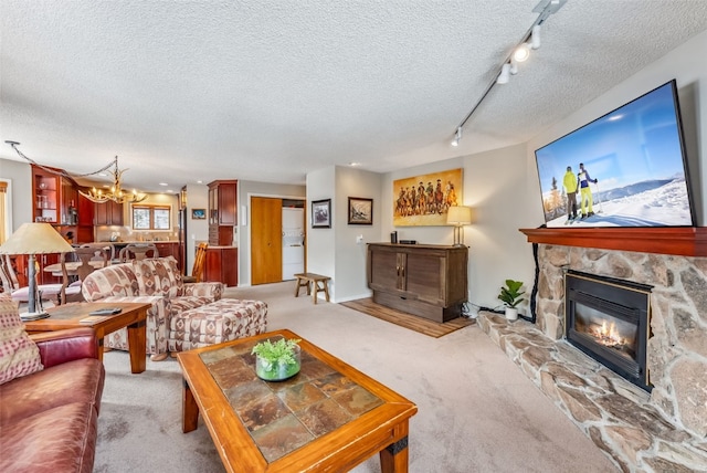 living room with a stone fireplace, light colored carpet, track lighting, and a textured ceiling