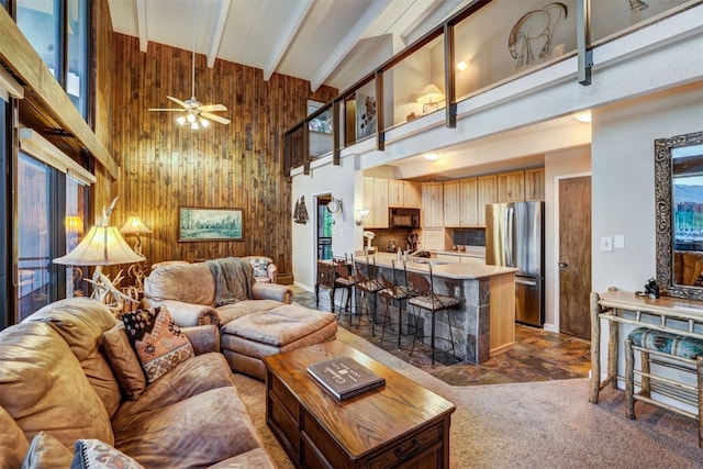 living room featuring beam ceiling, high vaulted ceiling, ceiling fan, and wood walls