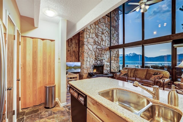 kitchen with sink, ceiling fan, a textured ceiling, a fireplace, and black dishwasher