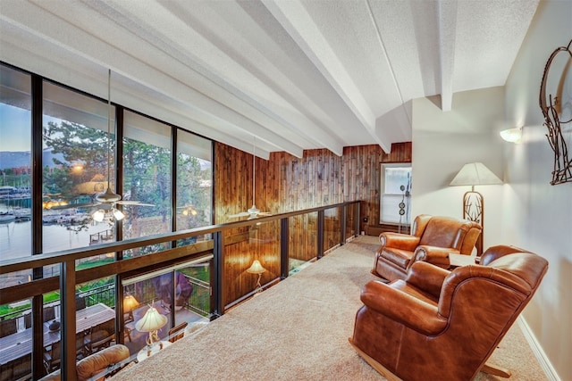 sitting room featuring carpet floors, lofted ceiling with beams, ceiling fan, and wood walls