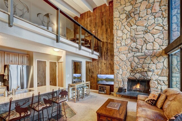 living room featuring carpet, beam ceiling, a towering ceiling, and wooden walls