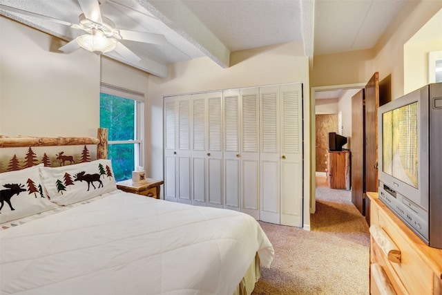 carpeted bedroom with beamed ceiling, ceiling fan, and a closet