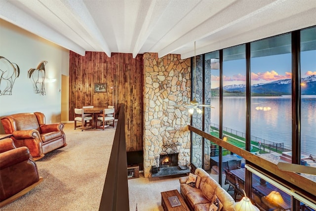 living room with a stone fireplace, beamed ceiling, a water view, wooden walls, and carpet