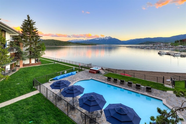 pool at dusk featuring a yard and a water and mountain view