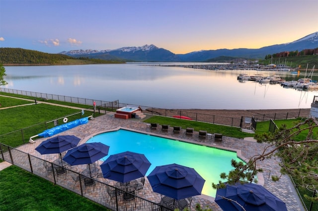 pool at dusk featuring a lawn and a water and mountain view