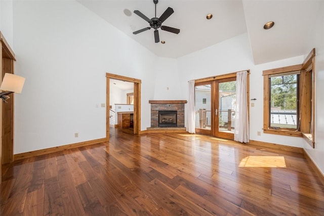 unfurnished living room with hardwood / wood-style floors, high vaulted ceiling, french doors, a stone fireplace, and ceiling fan