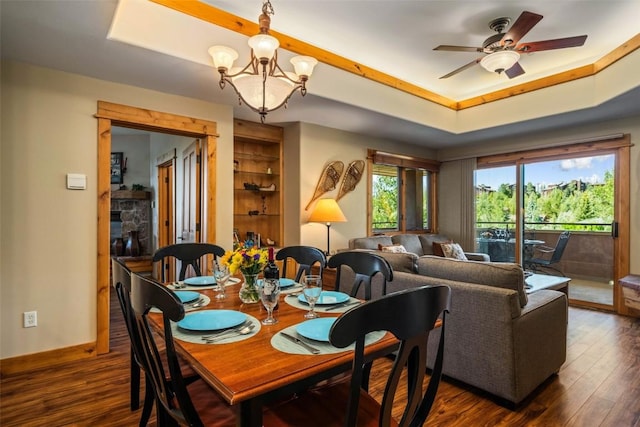 dining area featuring built in features, dark hardwood / wood-style flooring, ceiling fan with notable chandelier, and a raised ceiling