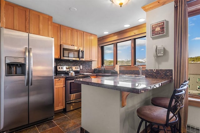 kitchen with sink, appliances with stainless steel finishes, tasteful backsplash, a kitchen bar, and kitchen peninsula