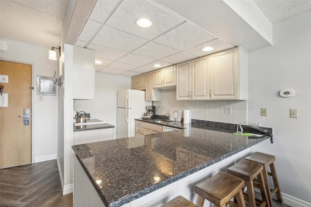 kitchen featuring kitchen peninsula, dark parquet flooring, white refrigerator, and dark stone countertops