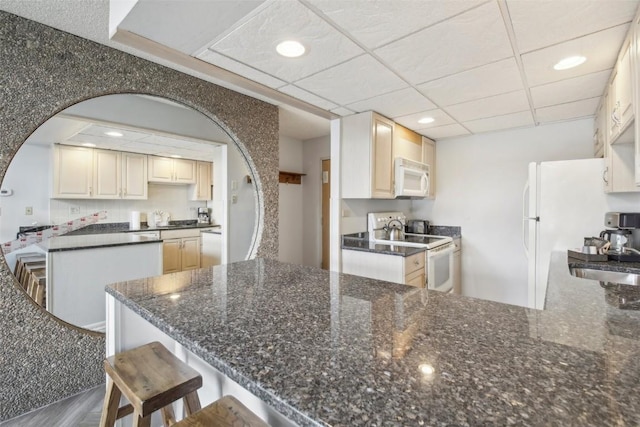 kitchen featuring kitchen peninsula, a paneled ceiling, white appliances, and a breakfast bar area