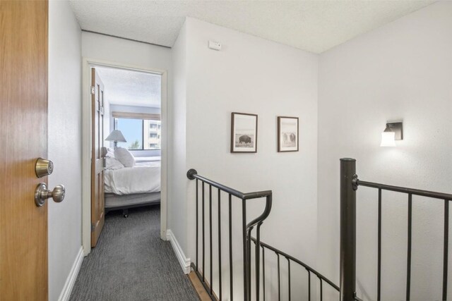 hall with a textured ceiling and dark colored carpet