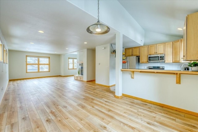 kitchen featuring a kitchen breakfast bar, open floor plan, stainless steel appliances, light wood-style floors, and baseboards