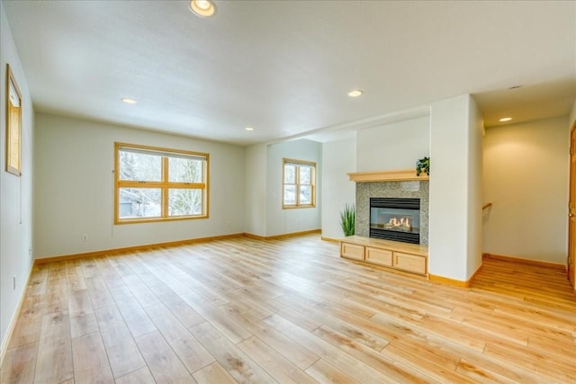 unfurnished living room with recessed lighting, a glass covered fireplace, light wood-style flooring, and baseboards